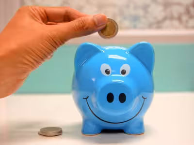Una mano metiendo una moneda en una hucha de cerdo azul
