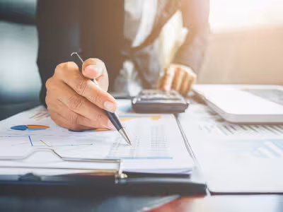 Una mano con un bolígrafo y un cuaderno de contabilidad junto a una calculadora